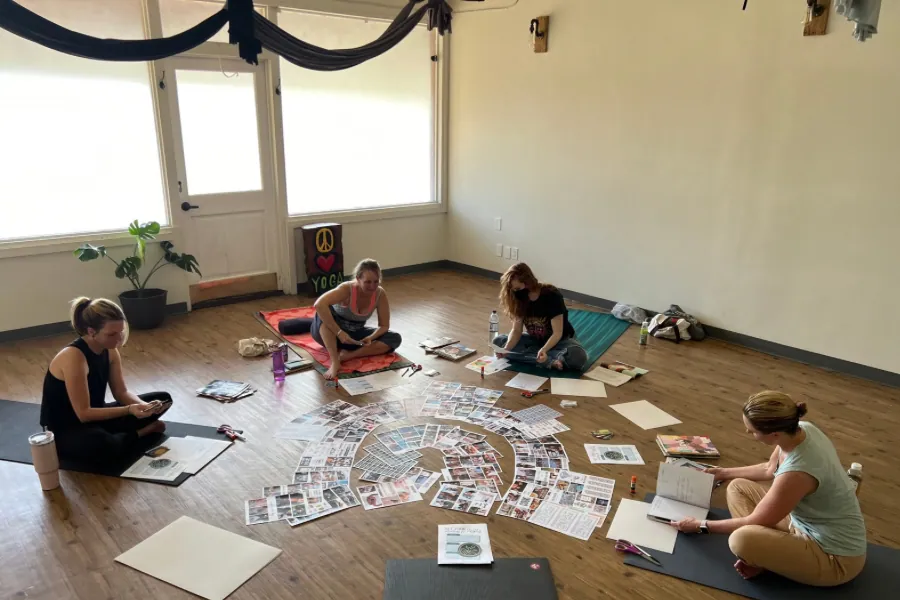 Four students seated in a circle over a spread of cards on the studio floor